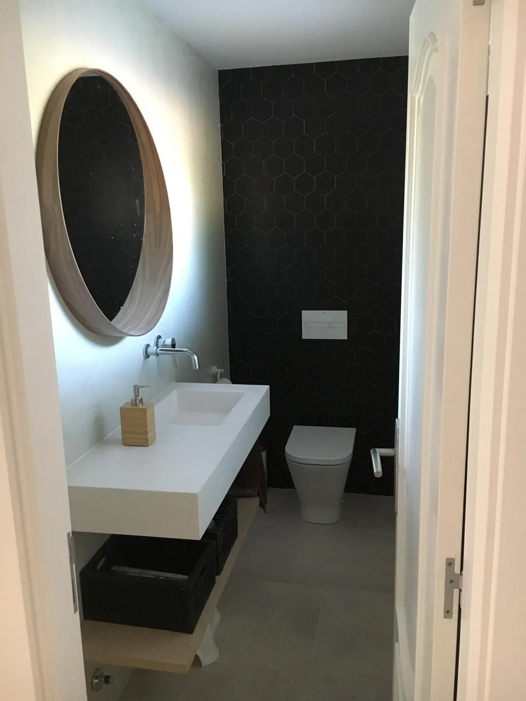 Baño reformado con papel pintado oscuro, espejo ovalado y mueble suspendido