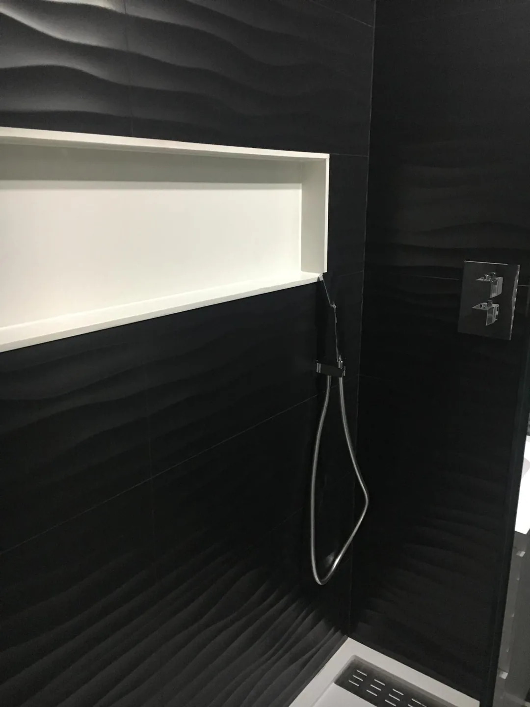 Ducha con revestimiento negro ondulado y hornacina iluminada