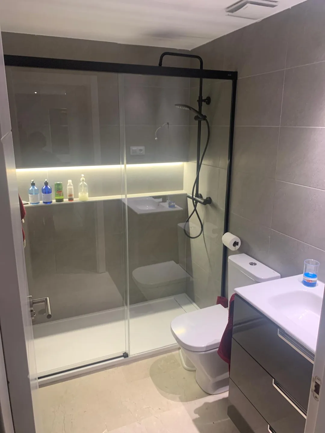 Baño con mampara corredera, ducha iluminada y mueble de madera